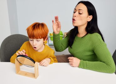 Speech therapist practicing gliding correction with a child using a mirror during speech therapy session.