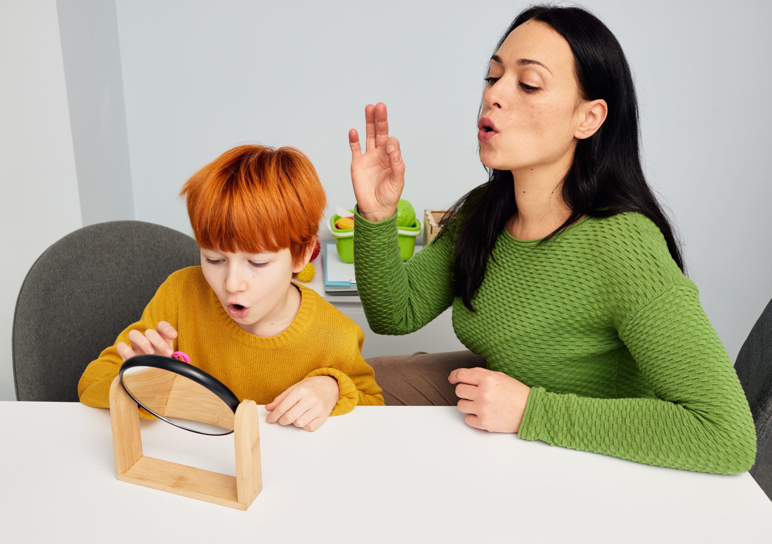 Speech therapist practicing gliding correction with a child using a mirror during speech therapy session.
